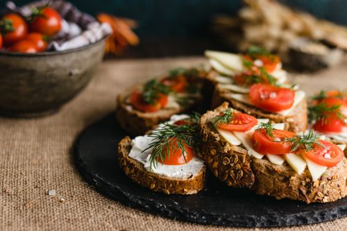 Free Artistic display of rustic bread slices topped with tomatoes, dill, and cheese on a slate plate, perfect for food photography. Stock Photo