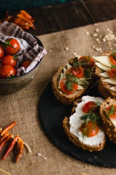 Savory multi-grain bread topped with cheese, cherry tomatoes, and dill on a rustic burlap setting.