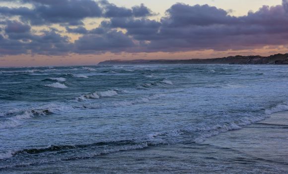 Stunning ocean waves rolling in under a dramatic sunset sky with dark clouds.