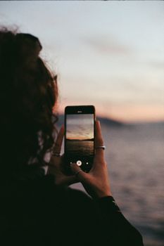 Silhouette of person photographing a sea sunset with a smartphone.