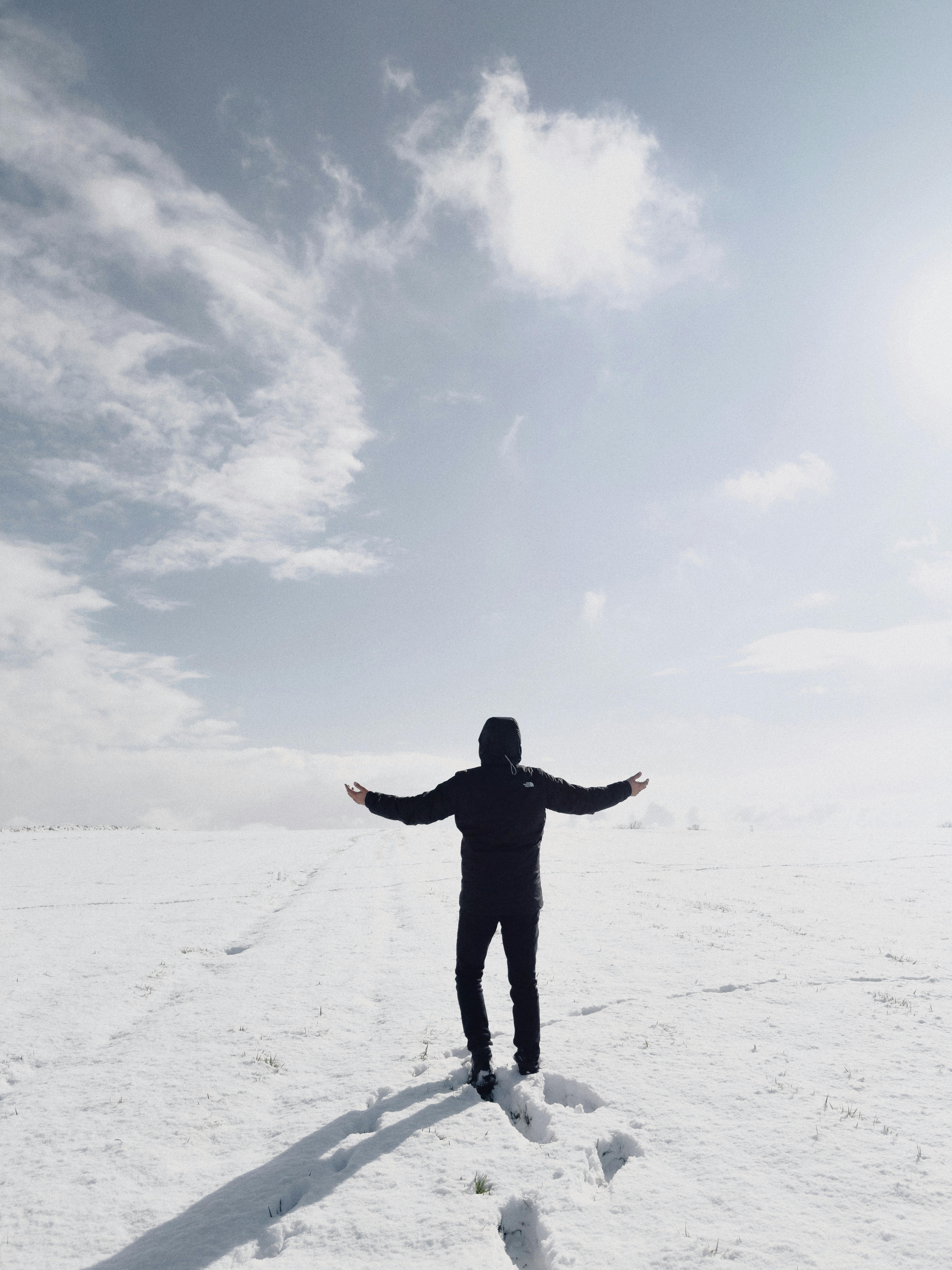 Person in winter attire stands alone in a snowy landscape, arms outstretched.