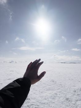 A dramatic image of a hand reaching towards the sun over a vast snowy landscape, expressing hope.
