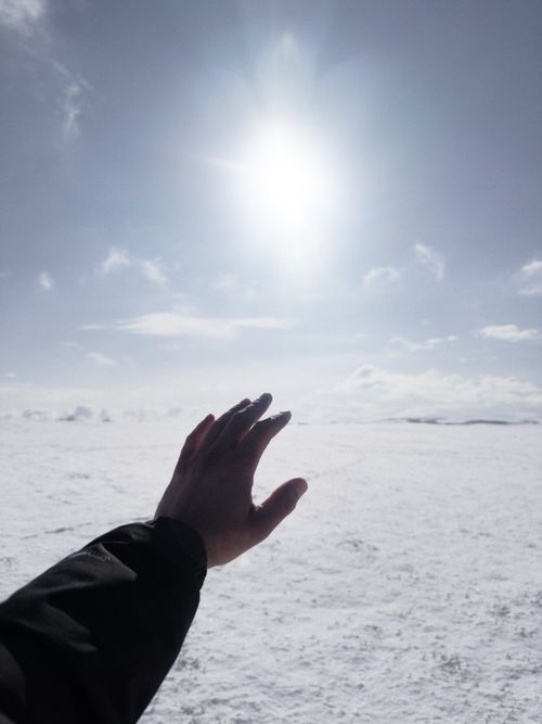 Free A dramatic image of a hand reaching towards the sun over a vast snowy landscape, expressing hope. Stock Photo