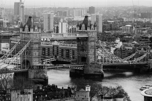 A dramatic black and white aerial view of London's iconic Tower Bridge and cityscape.