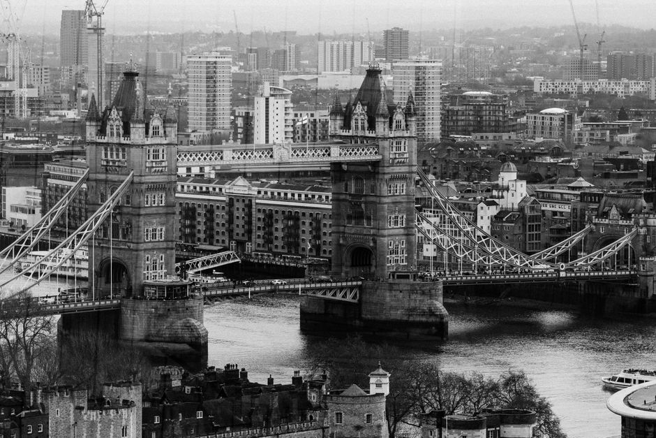 A dramatic black and white aerial view of London's iconic Tower Bridge and cityscape.
