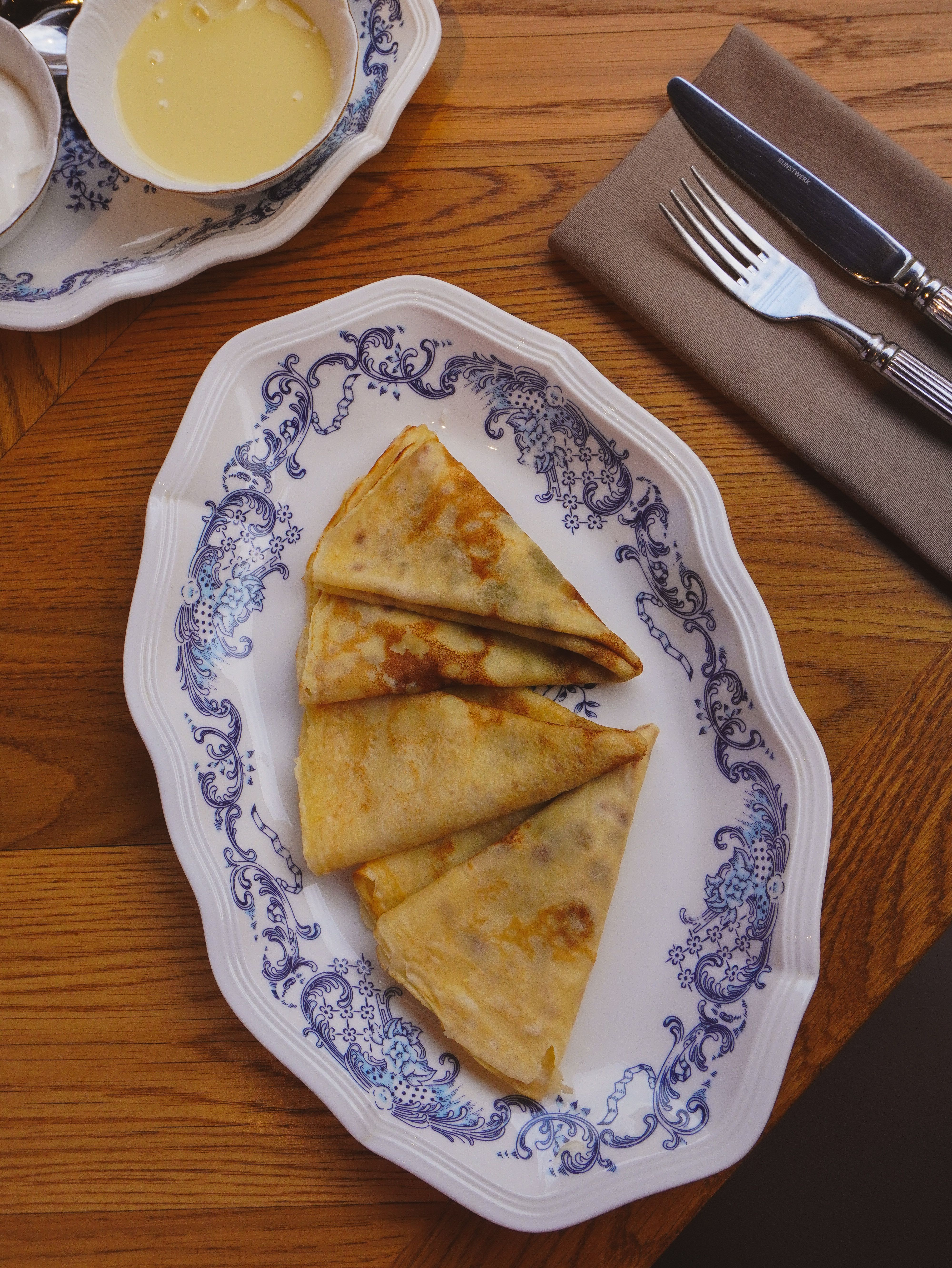 Tasty crepes beautifully plated on ornate porcelain with syrup and cutlery.