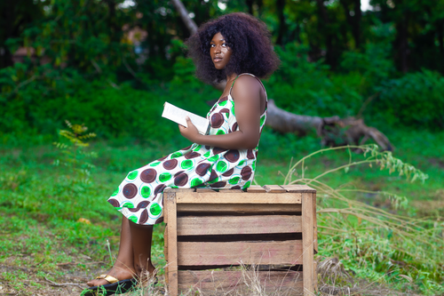 Free Young African woman reading outdoors in a vibrant green setting. Stock Photo