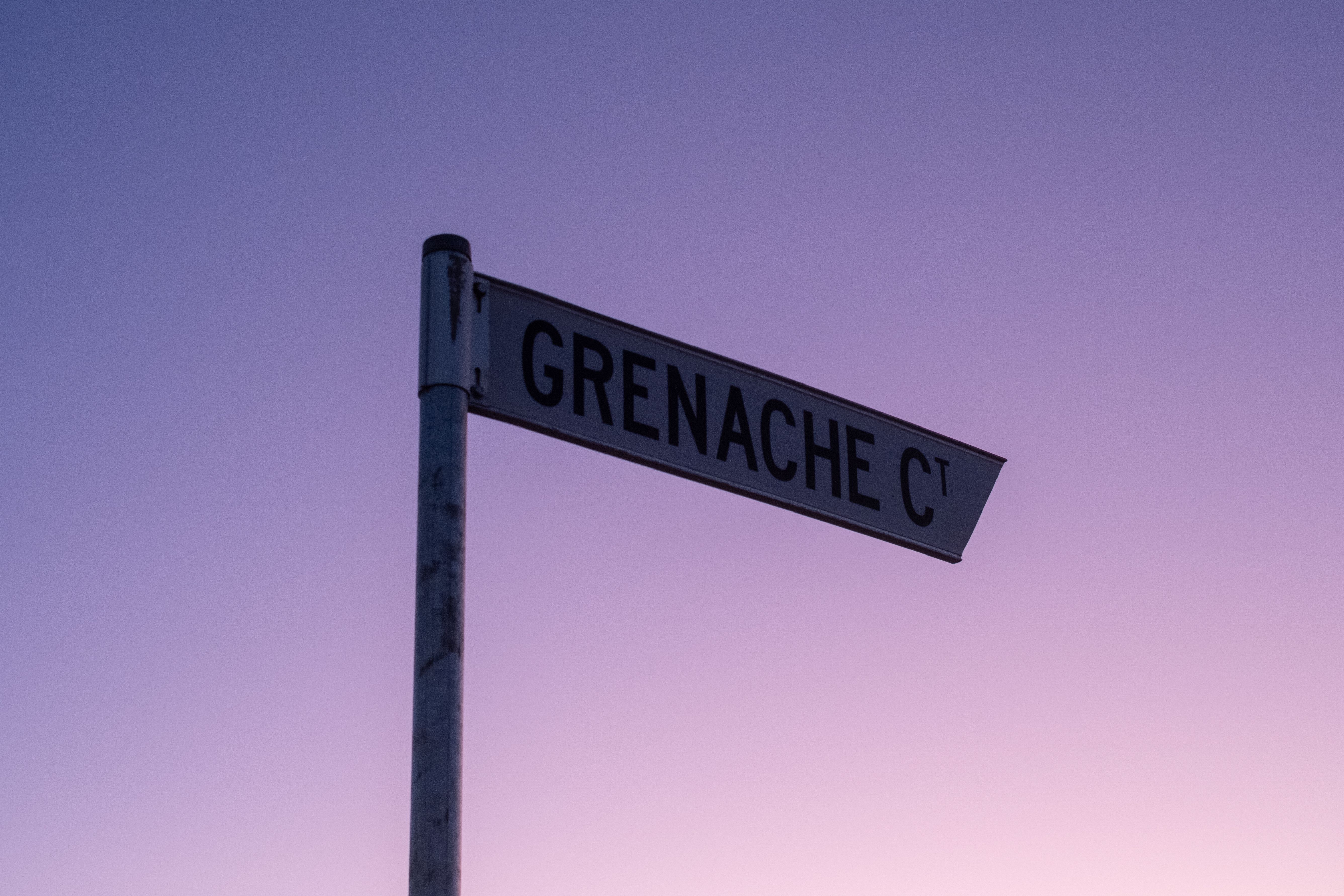 Street sign labeled Grenache Ct silhouetted against a soft purple twilight sky.