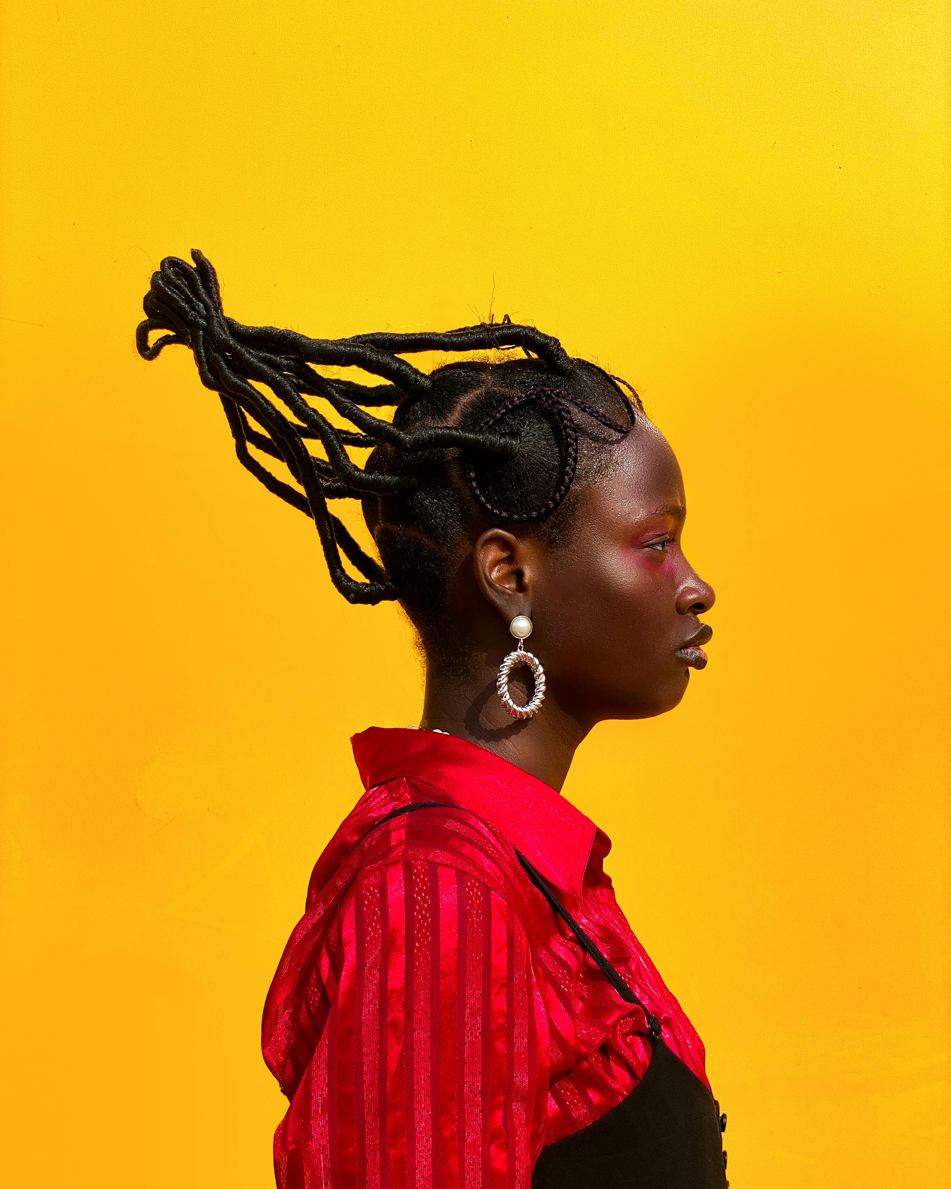 Side profile of a stylish woman in a red outfit with braided hair against a vivid yellow background.