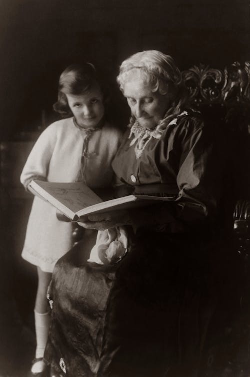 Free Old Woman Sitting on Chair And Reading A Book To A Child Stock Photo