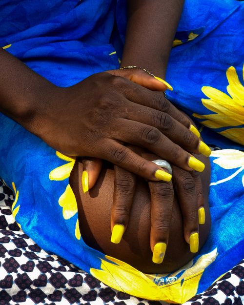 Free Detailed close-up of hands with bright yellow nail polish set against vibrant blue fabric with floral patterns. Stock Photo