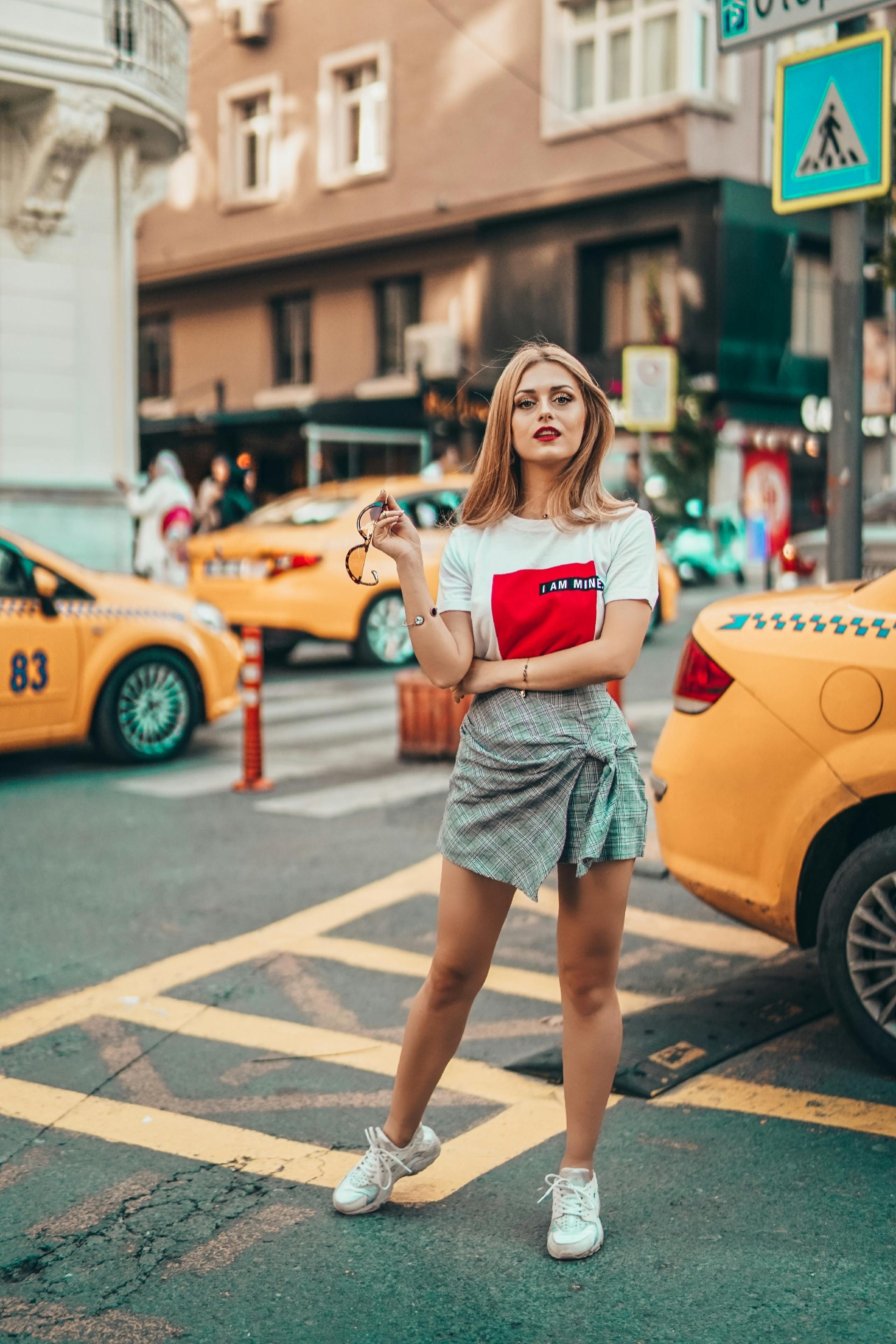 Stylish woman in casual wear posing at a busy street in Istanbul with yellow taxis around.
