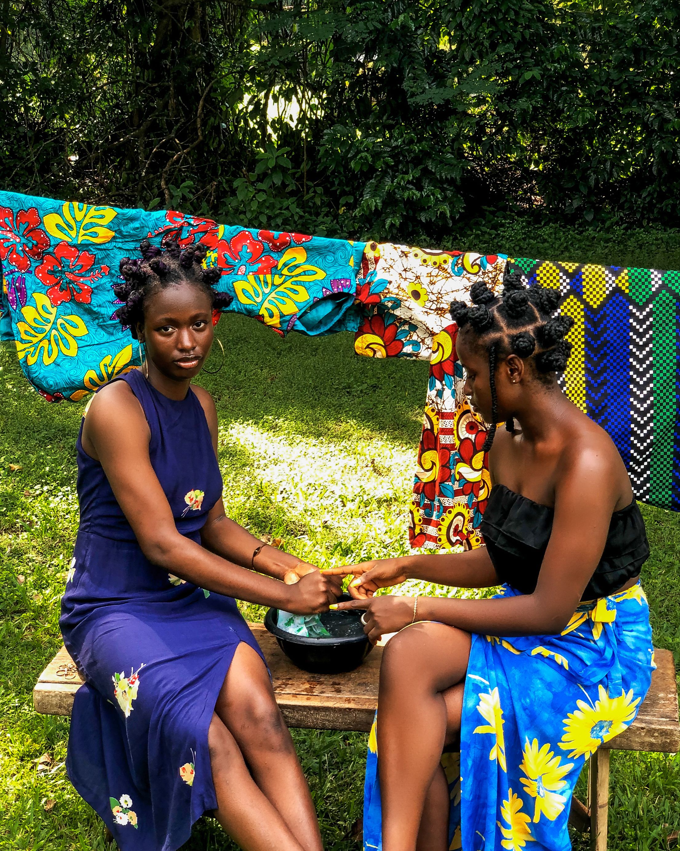 Two women outdoors with traditional hairstyles, engaging in cultural activity.