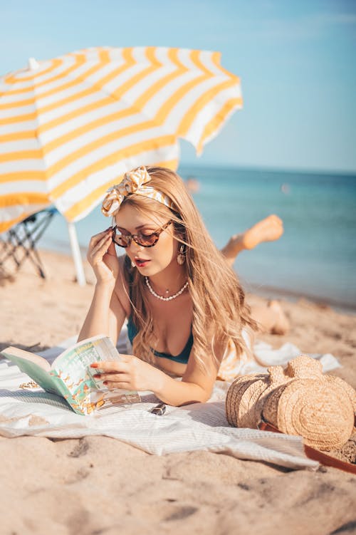 Women's lying on the beach sand reading a book
