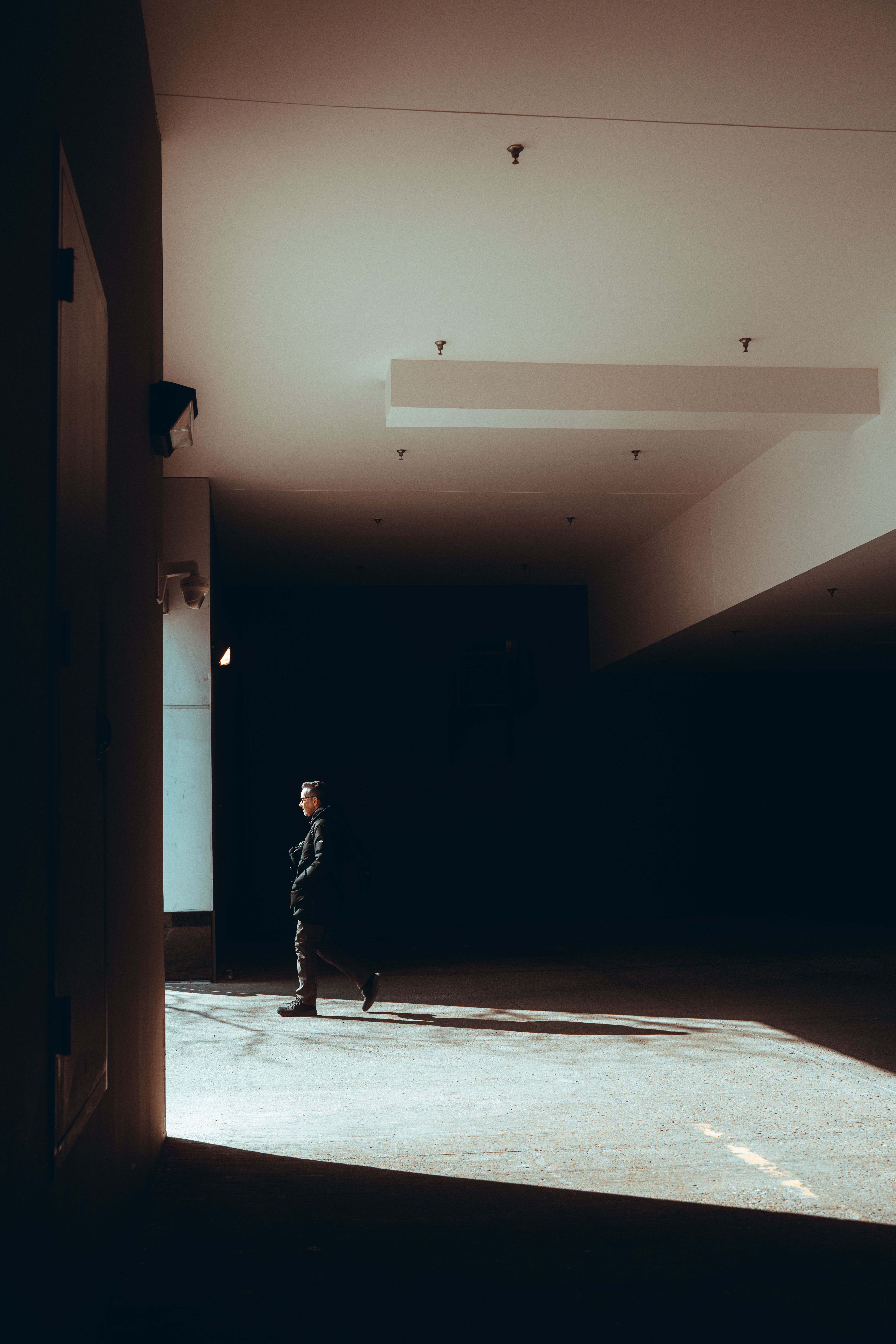 Silhouette of a person walking in a dimly lit urban corridor with striking light and shadow contrast.