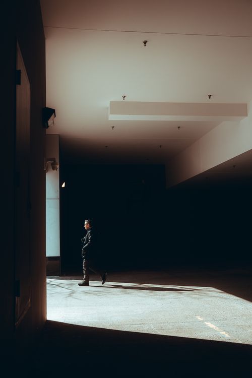 Free Silhouette of a person walking in a dimly lit urban corridor with striking light and shadow contrast. Stock Photo