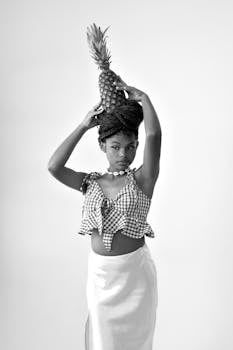 Artistic black and white portrait of a woman balancing a pineapple, showcasing elegance.