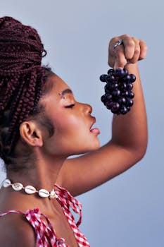 Portrait of a young woman holding a bunch of grapes with vibrant expression.