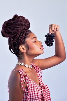 Young woman in checkered dress holding grapes against a neutral background.