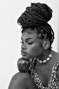 Stylish portrait of a woman with braided hair and an apple, in grayscale.