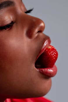Artistic close-up of woman's lips with a strawberry, emphasizing sensuality and freshness.