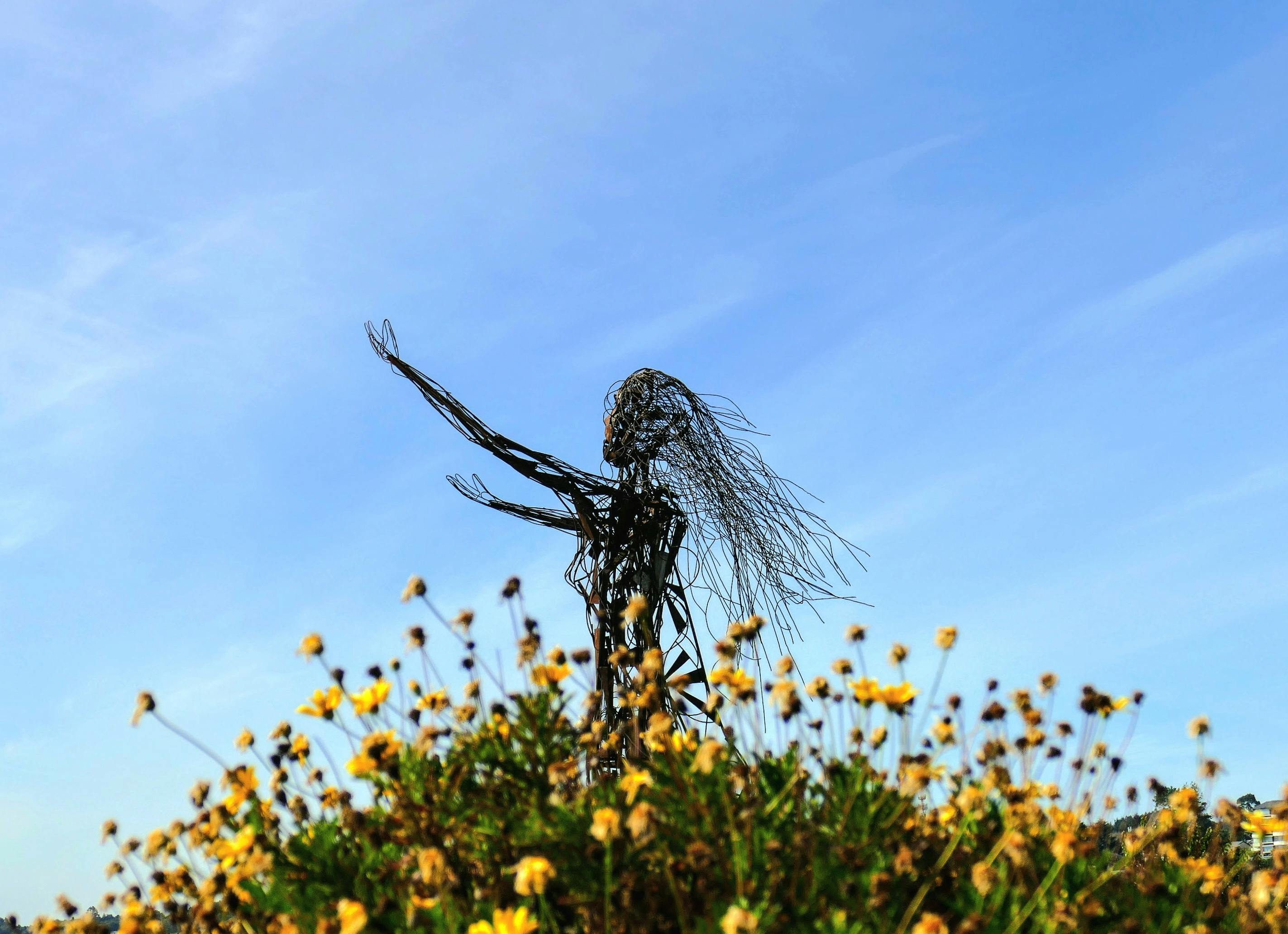 Artistic sculpture amidst yellow flowers under a clear blue sky in Puerto Varas, Chile.