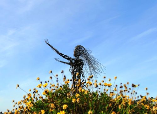 Free Artistic sculpture amidst yellow flowers under a clear blue sky in Puerto Varas, Chile. Stock Photo