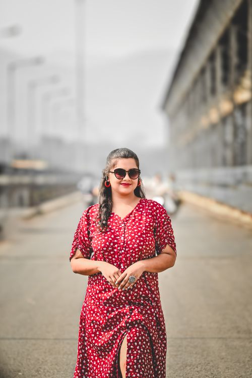 Free Confident woman in red dress posing outdoors with a backdrop of a bridge in Jharkhand, India. Stock Photo