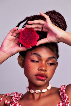 Stylish portrait of a young woman holding a vibrant red fruit, showcasing modern beauty and fashion.