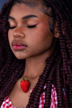 Close-up portrait of a woman with braided hair and a strawberry necklace, in a stylish setting.