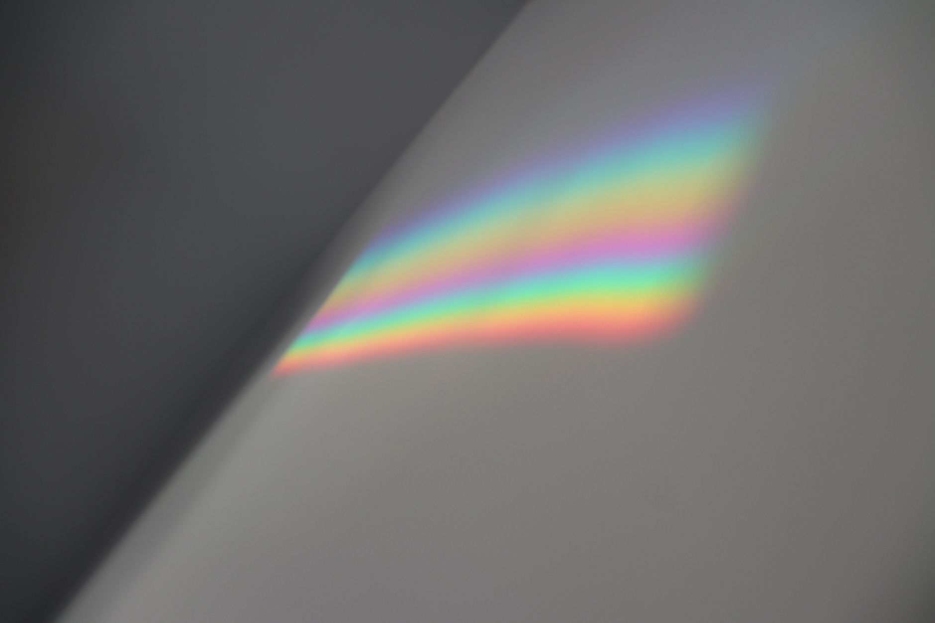 Soft rainbow light spectrum reflected on a neutral grey wall indoors.