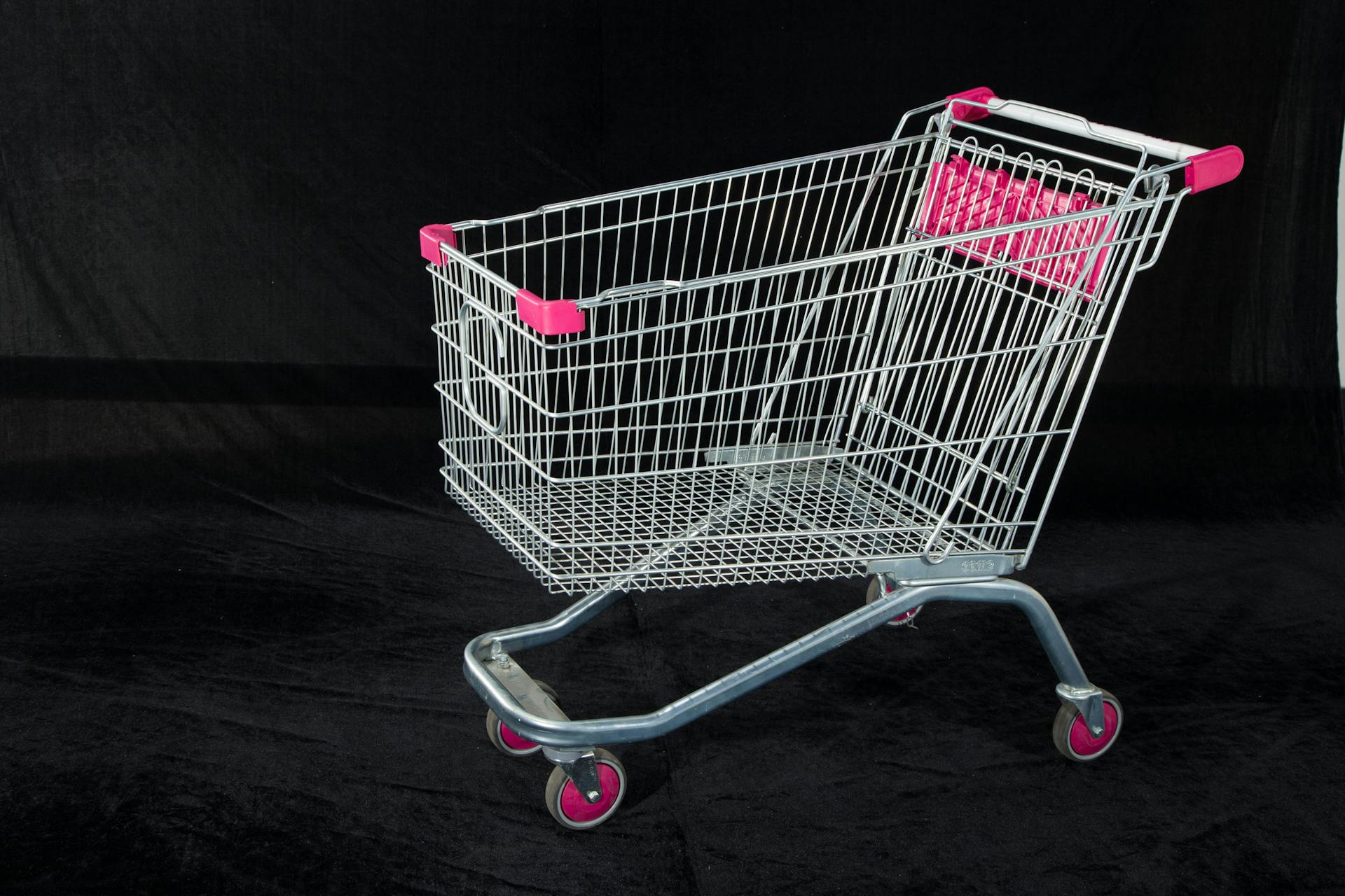 A metal shopping cart with pink handles and wheels on a dark backdrop, ideal for retail and commerce themes.