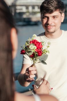 A man offering a bouquet of red flowers by the water in Buenos Aires, Argentina.