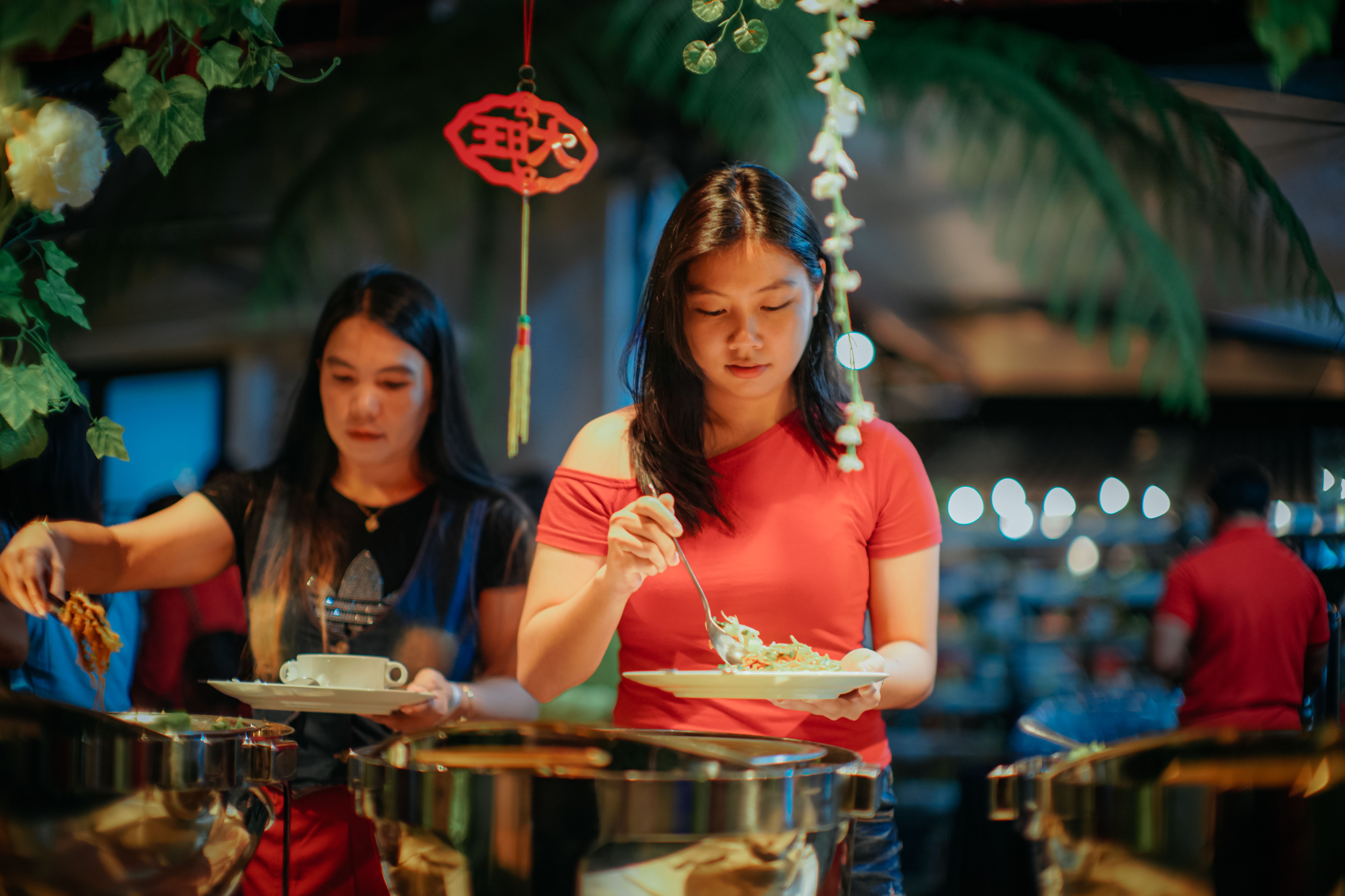 Two women serving themselves food from a buffet, in a festive and vibrant atmosphere.
