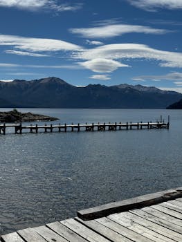 Serene view of a wooden pier extending into a tranquil lake with mountain backdrop in Neuquén, Argentina.