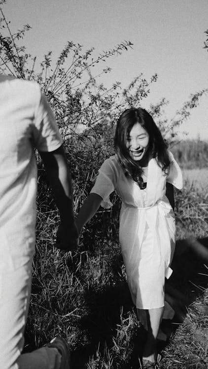 Black and white cheerful ethnic female holding hand with boyfriend and following crop man on summer day in nature
