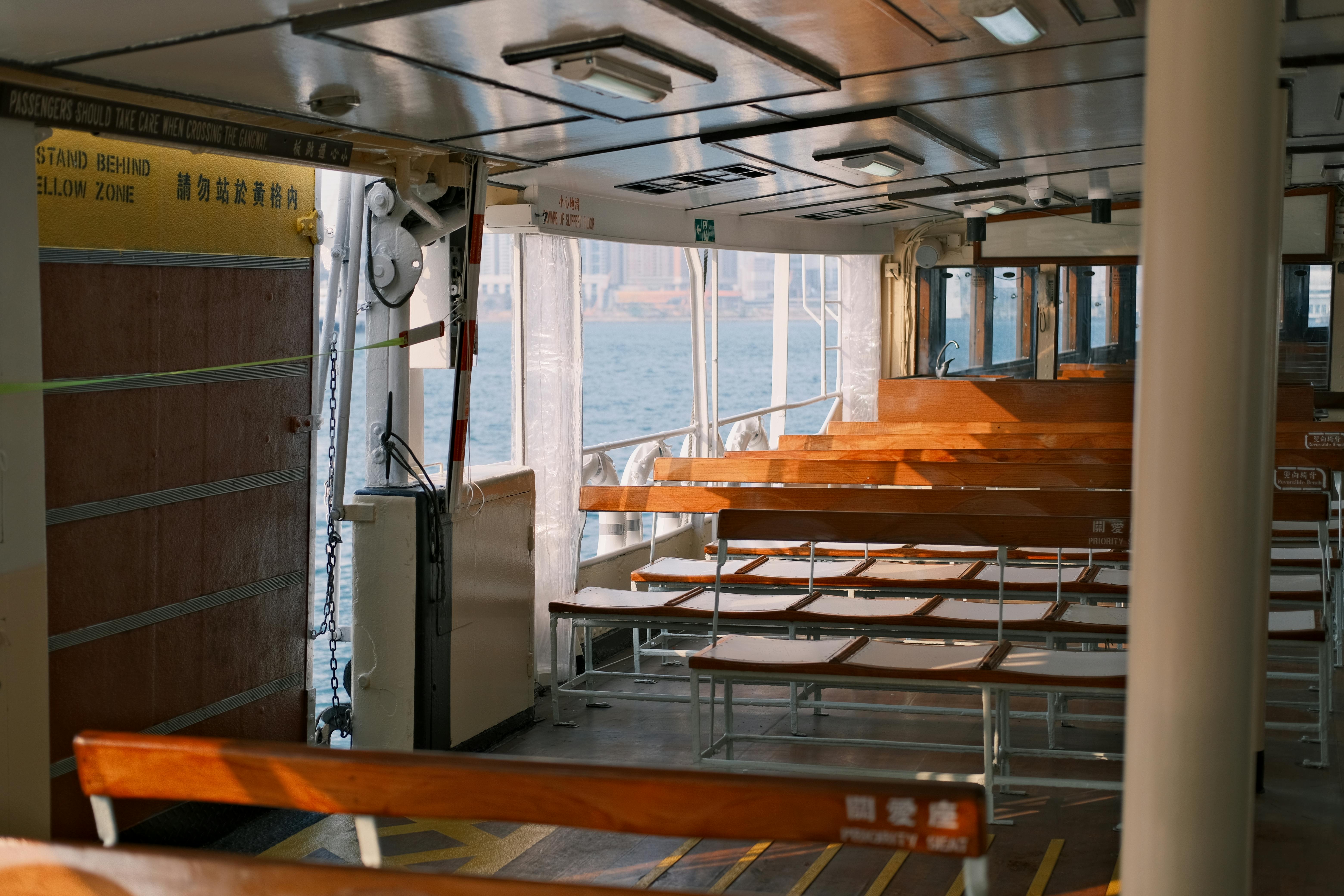 Interior view of a passenger ferry with wooden benches, overlooking the sea under daytime light.