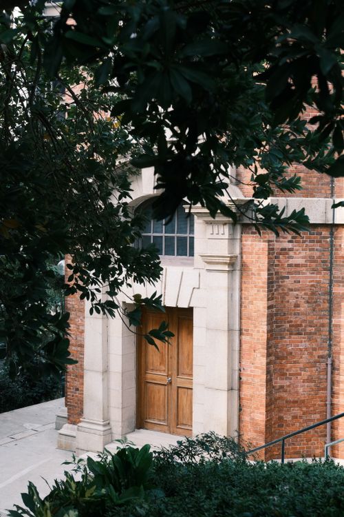 Free A rustic brick building entrance embraced by lush greenery, offering a calm and historic feel. Stock Photo
