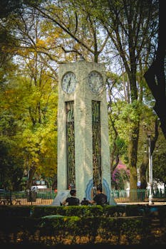 Timeless charm of a historic clock tower surrounded by lush trees in a Mexico City park.