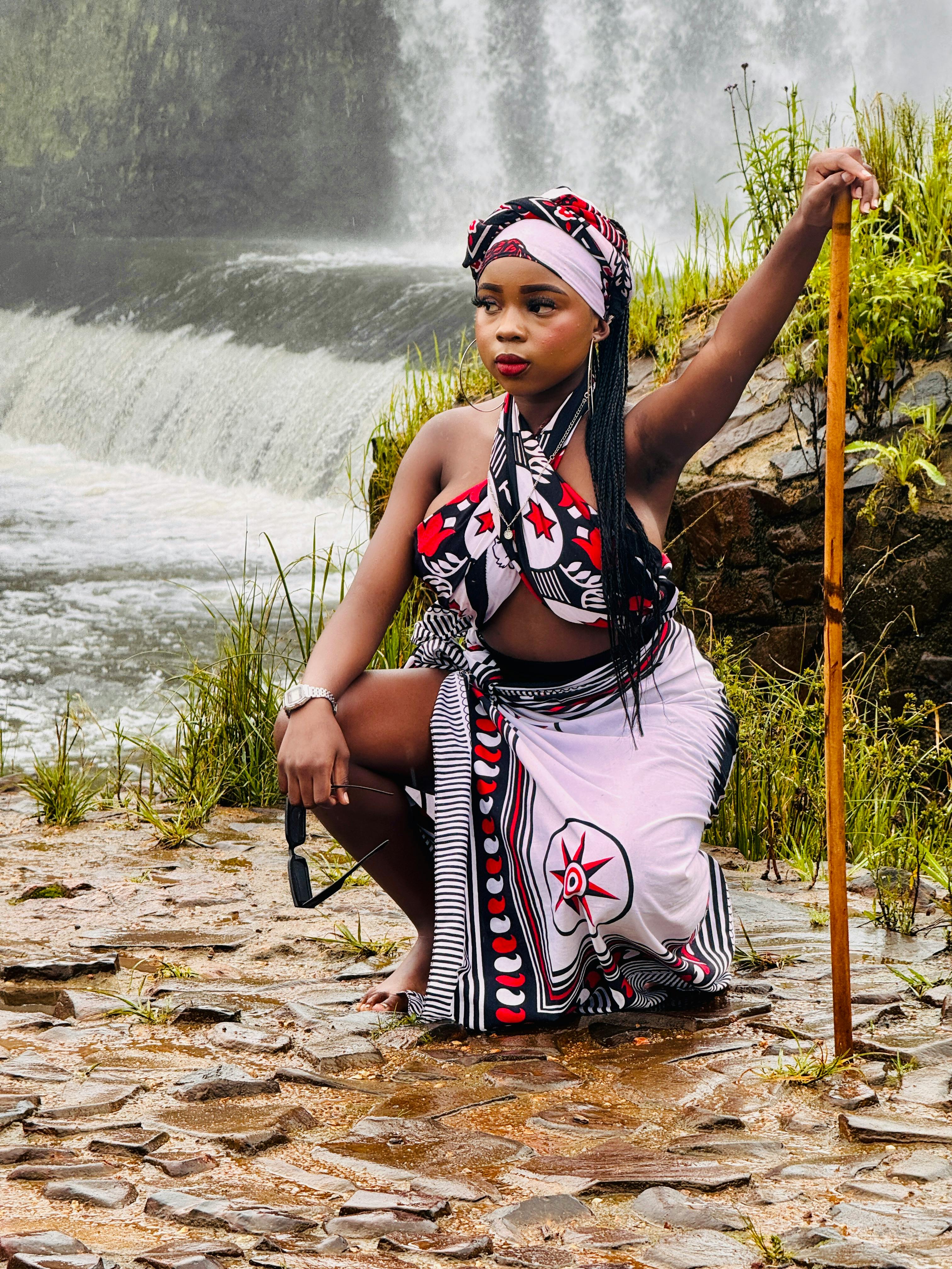 A woman in traditional attire poses elegantly by a picturesque waterfall.