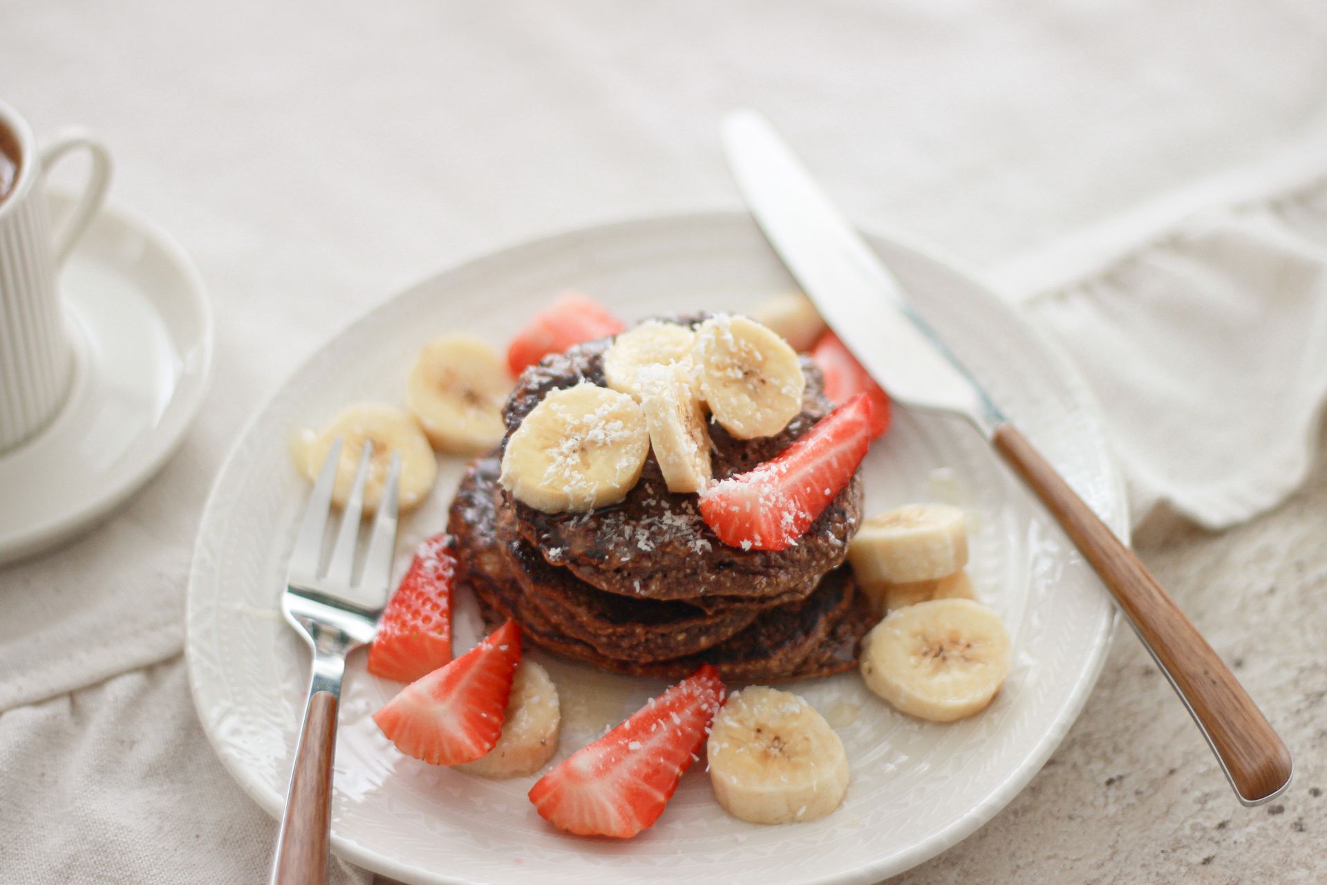 Tasty chocolate pancakes topped with strawberries, bananas, and coconut flakes, perfect for a sweet breakfast.