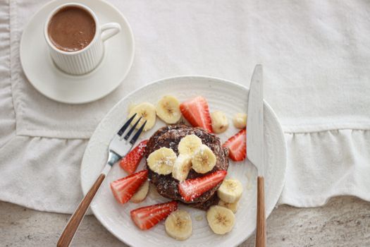 A mouth-watering breakfast featuring pancakes topped with bananas and strawberries and a hot chocolate.