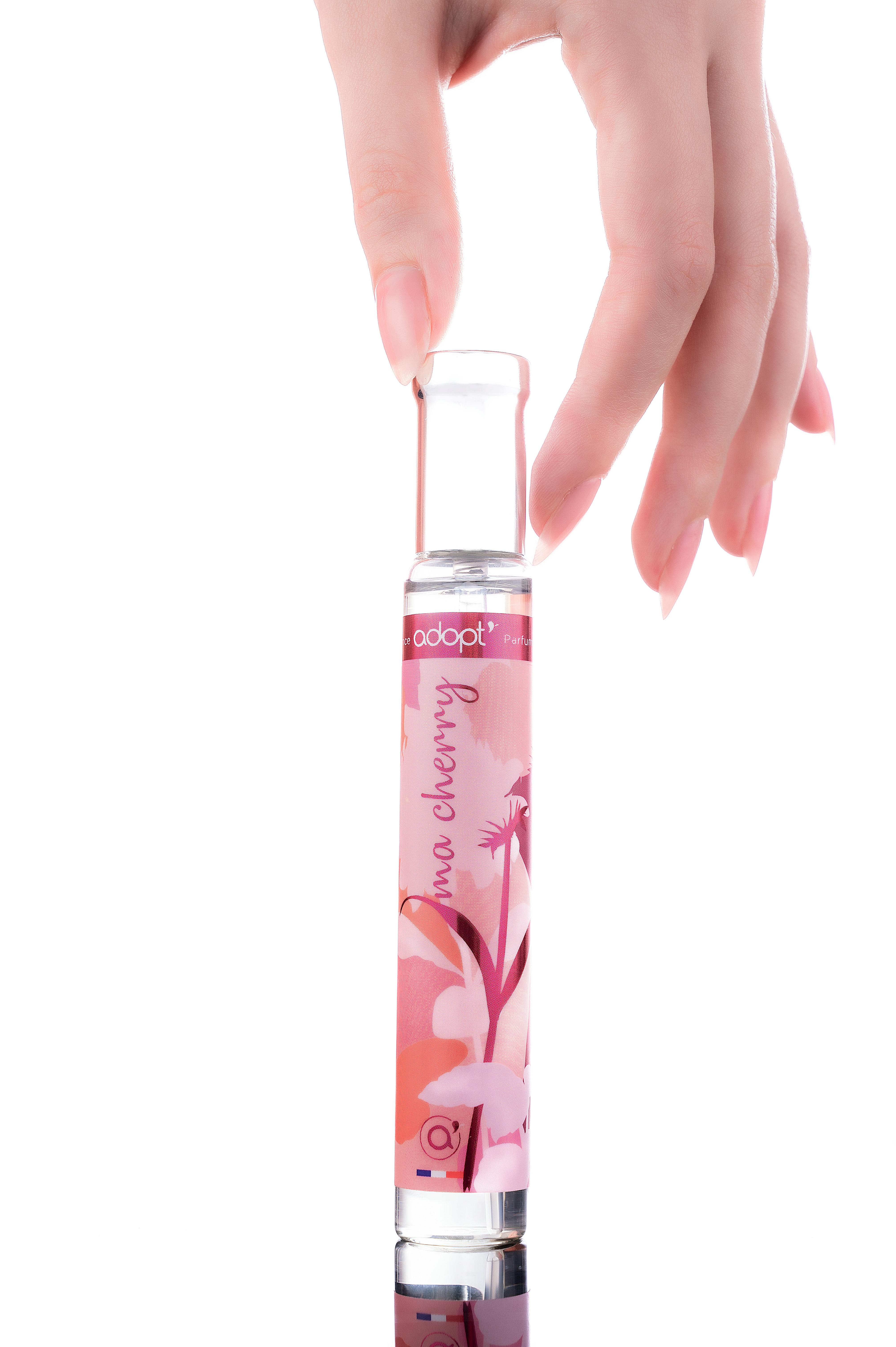 A hand gracefully holds a cherry blossom fragrance bottle against a white background.