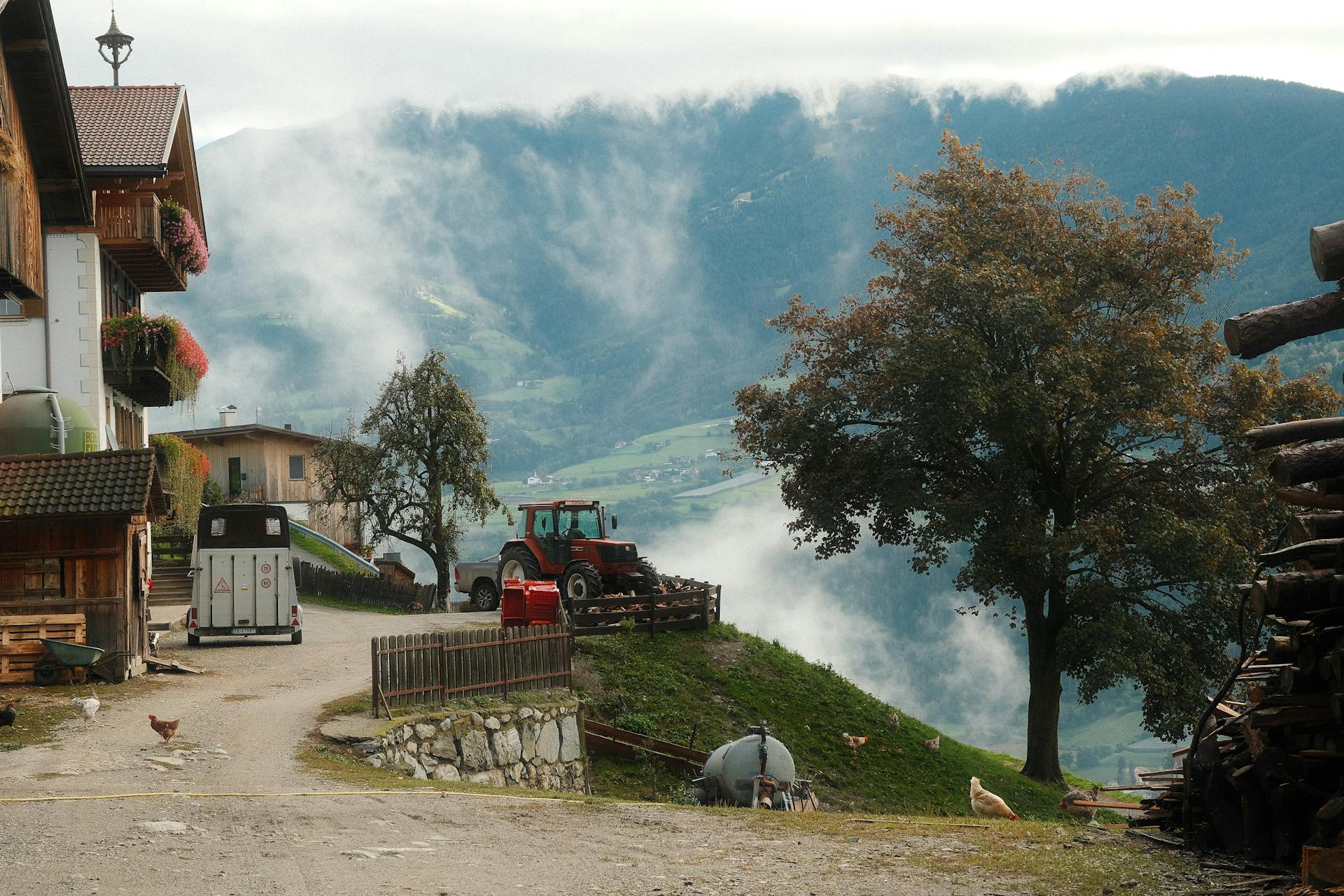 Picturesque rural farm scene with a tractor, chickens, and misty mountains.