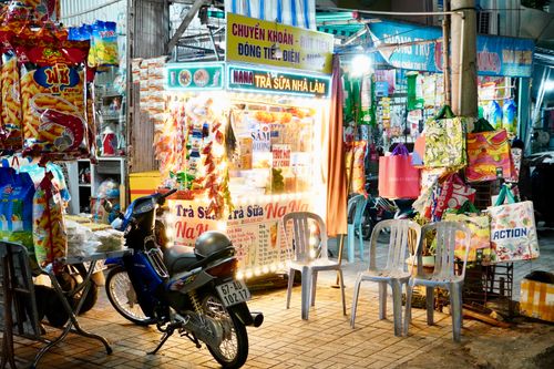 Free Colorful street vendor stall at night market with hanging snacks and plastic chairs, Vietnam. Stock Photo