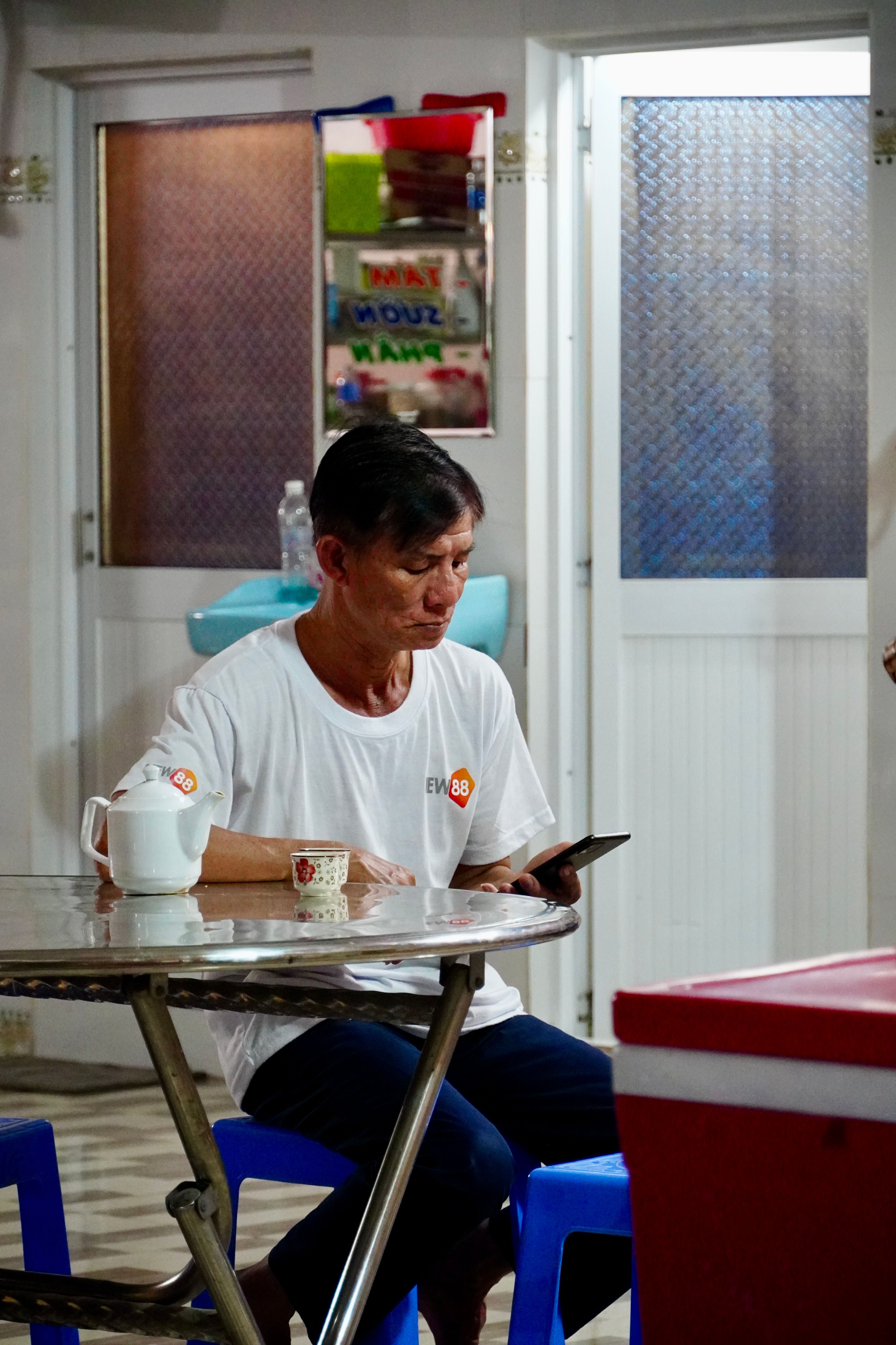 A man seated at a table, engaged with his smartphone in a casual indoor setting.