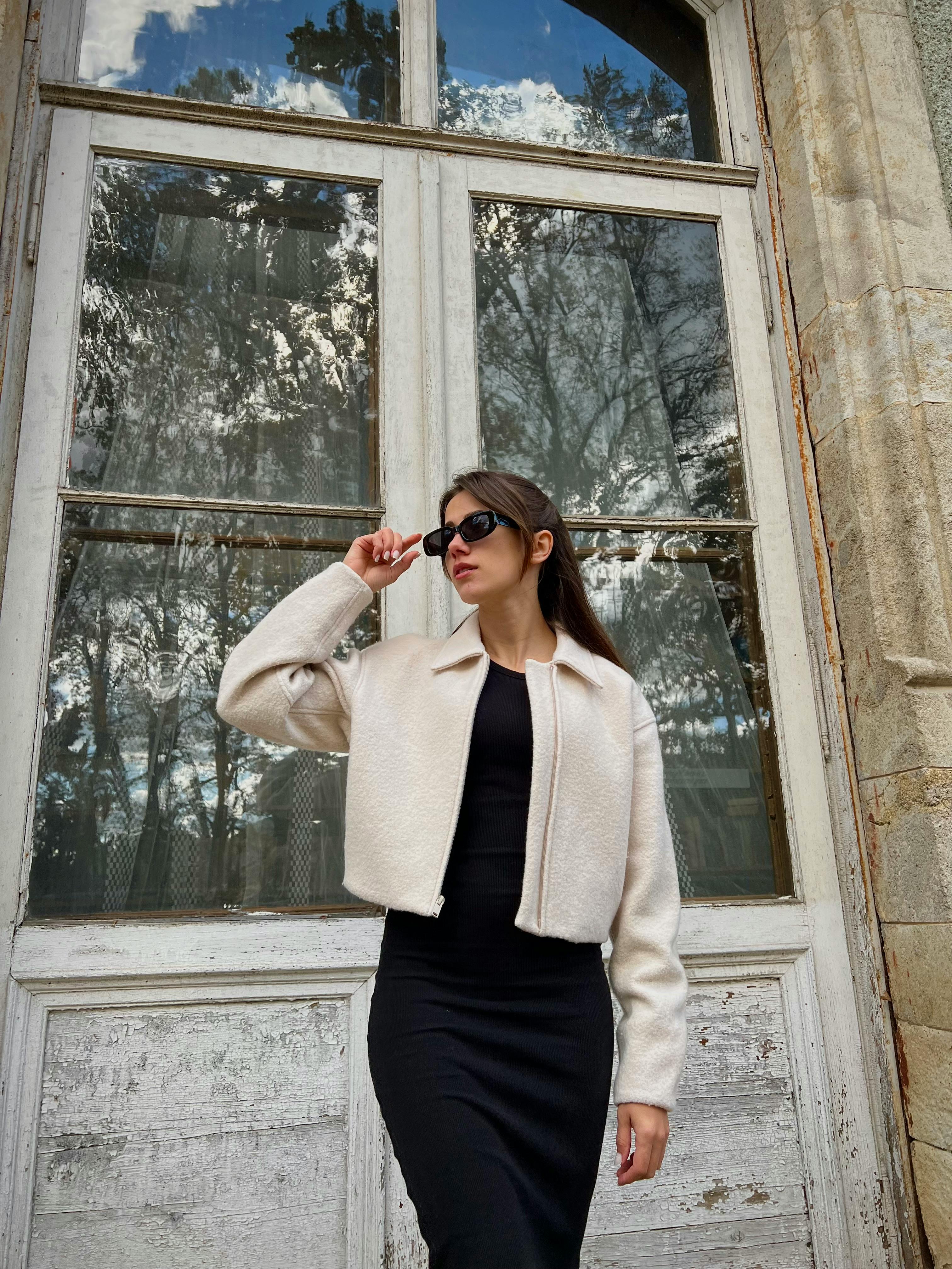 Stylish woman in a classy outfit posing confidently by a vintage window.