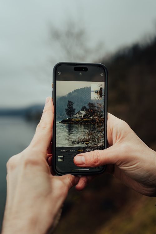 Free A person taking a scenic lake photo with a smartphone on a cloudy day. Stock Photo