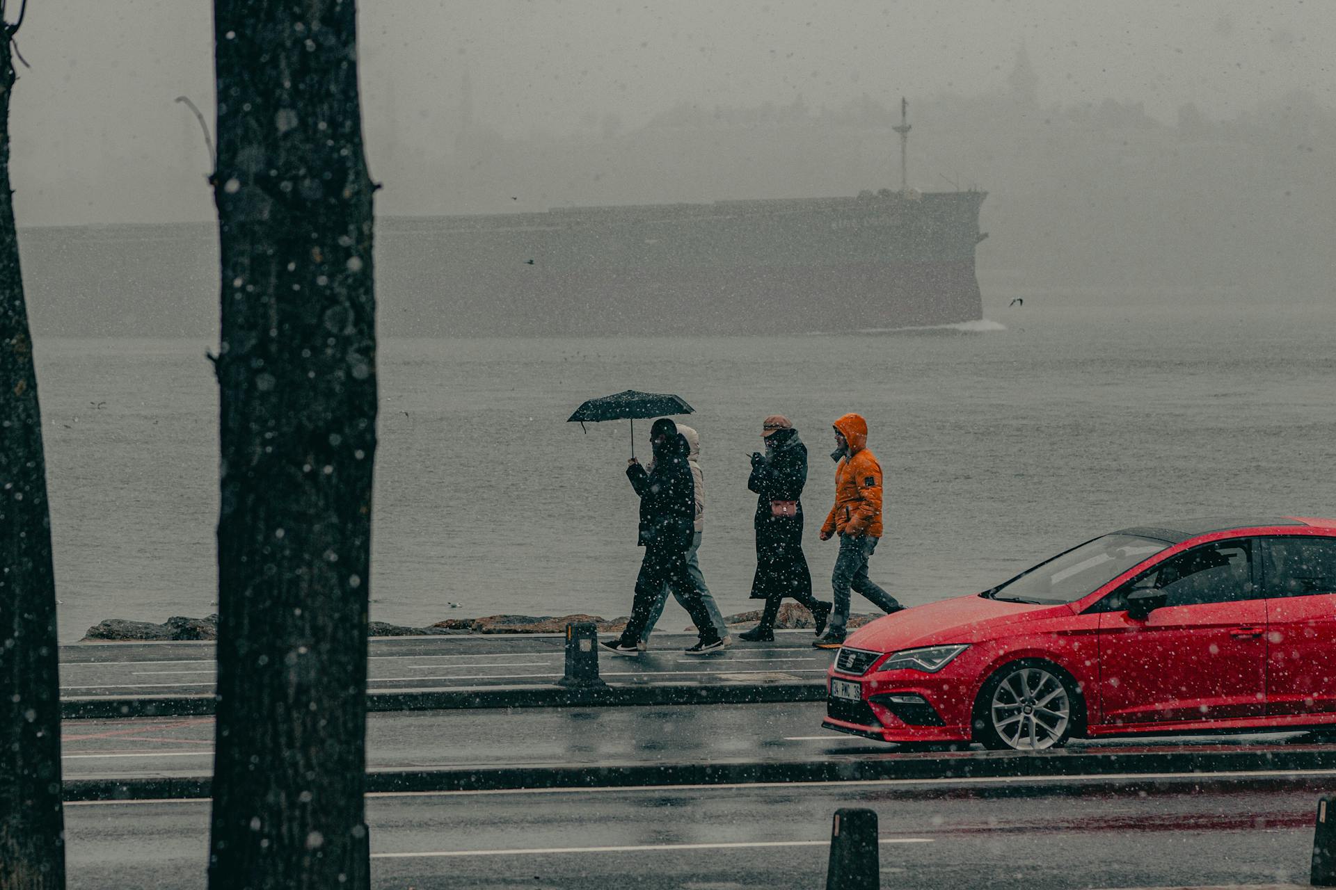 Snowy day in Istanbul with pedestrians and red car by the waterfront.