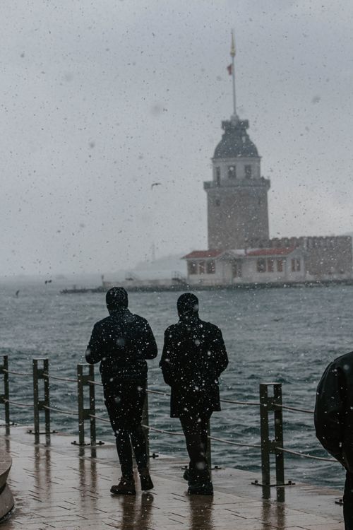 Free Two people stand by the Bosphorus with Maiden's Tower in the background during a snowy day in Istanbul. Stock Photo